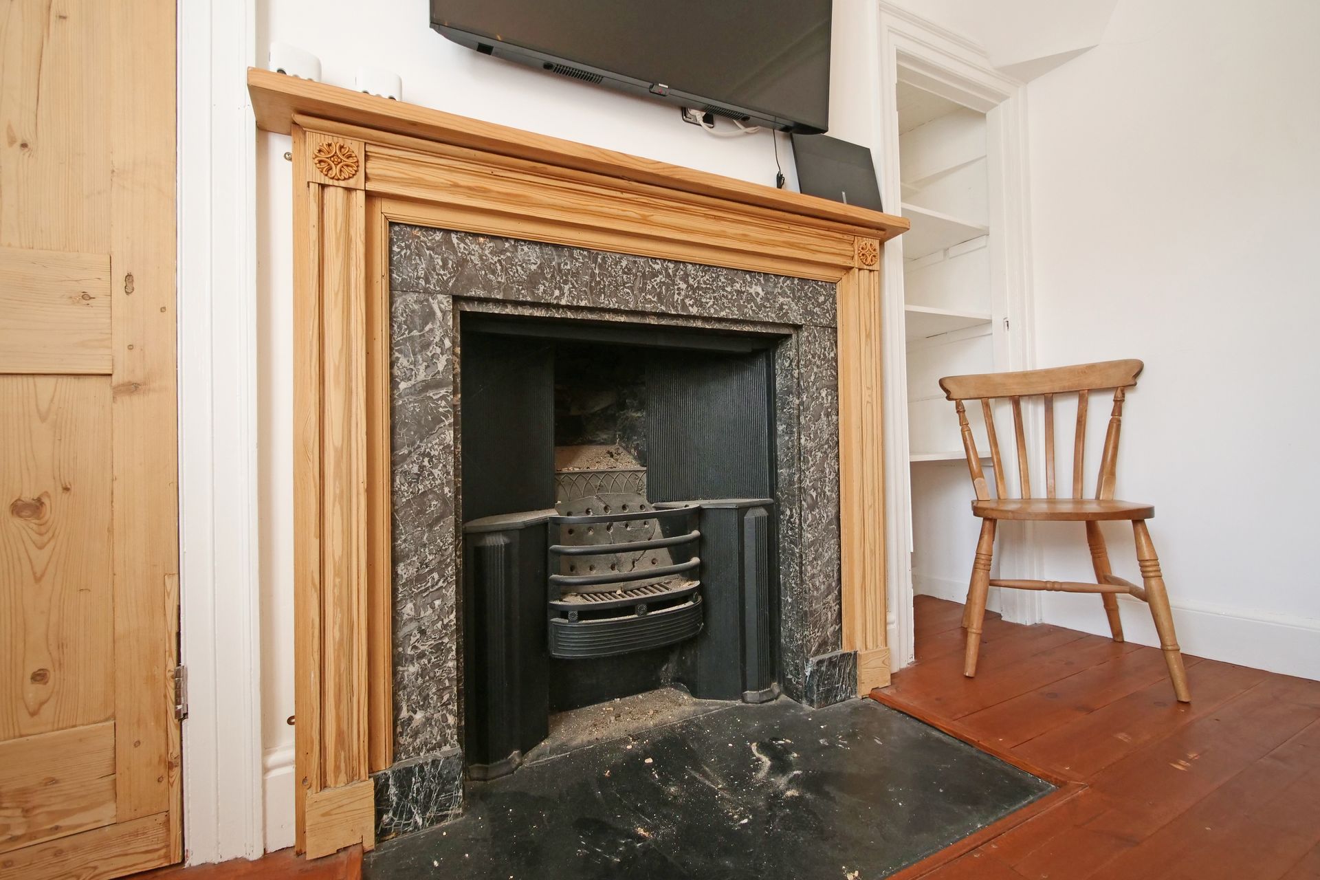 Fireplace with a wooden mantel and black marble surround. A wooden chair sits nearby.