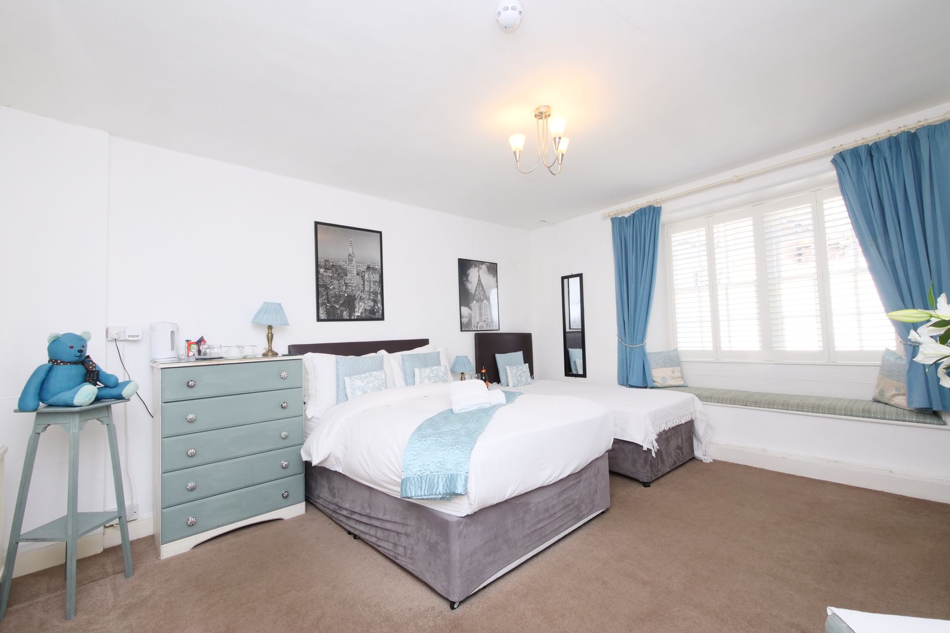 Bedroom with a king-size bed, single bed, blue dresser, curtains, and a stuffed animal.