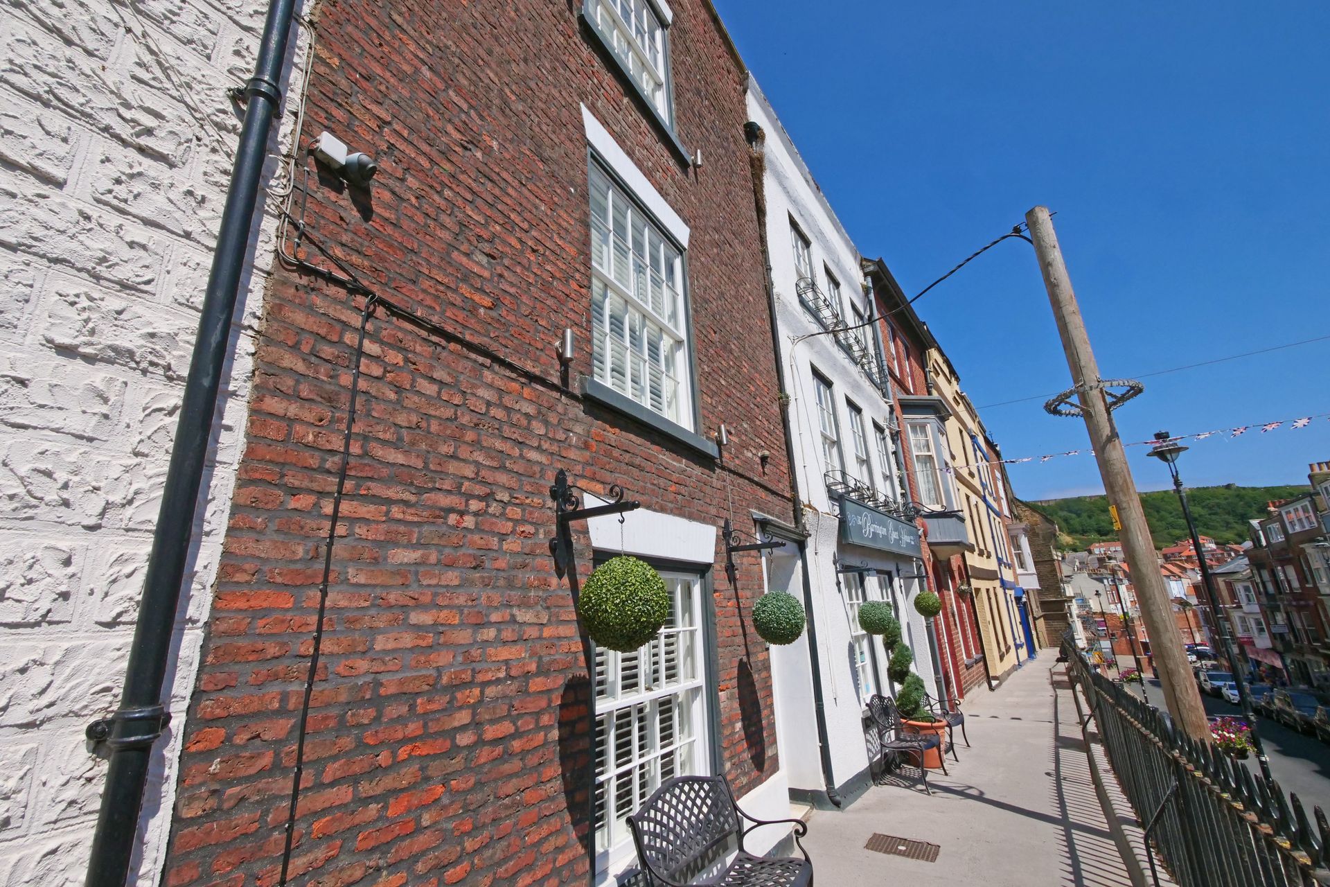 Brick building exterior with white window frames, along a walkway in a sunny street. 