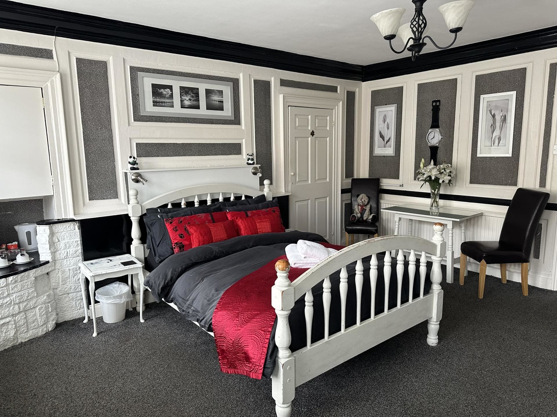 A bedroom with a white bed, dark bedding, and red pillows and throw. 