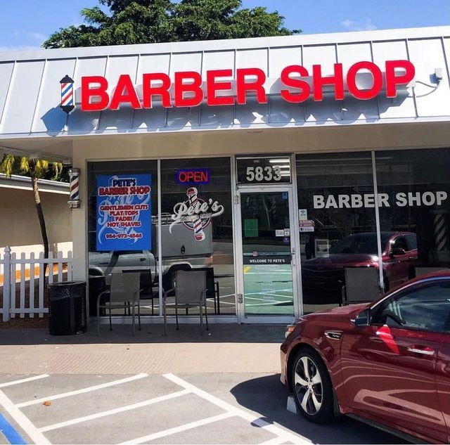 A red car is parked in front of a barber shop