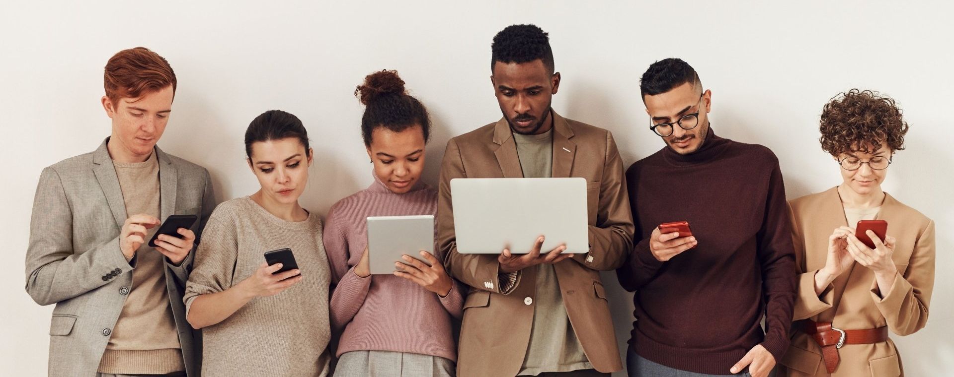 a group of people are standing next to each other looking at their phones and laptops .