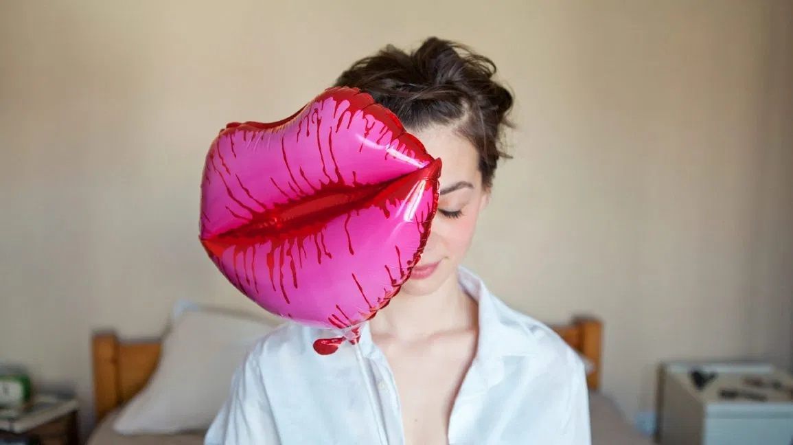 A woman is holding a balloon in the shape of lips in front of her face.