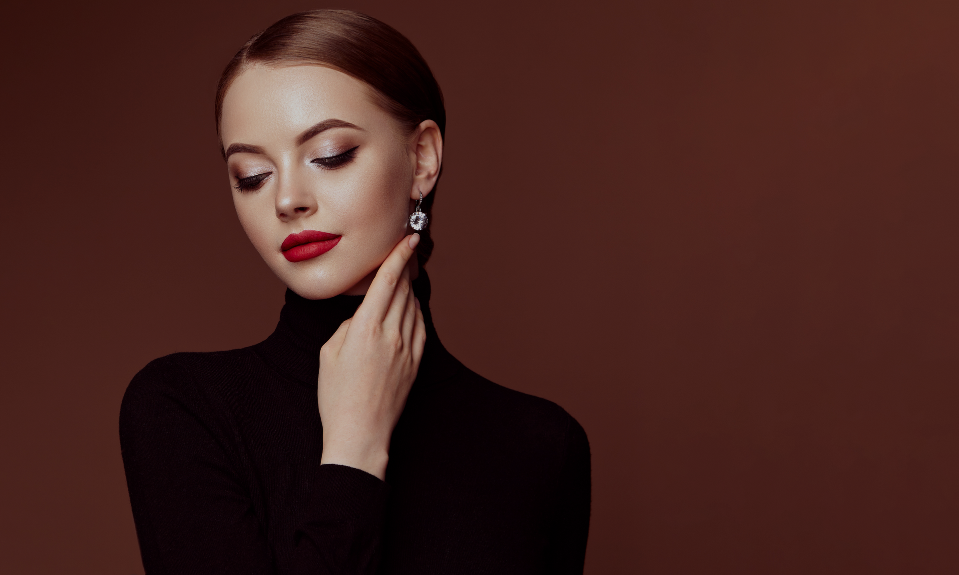 A woman wearing a black turtleneck and red lipstick is touching her neck.