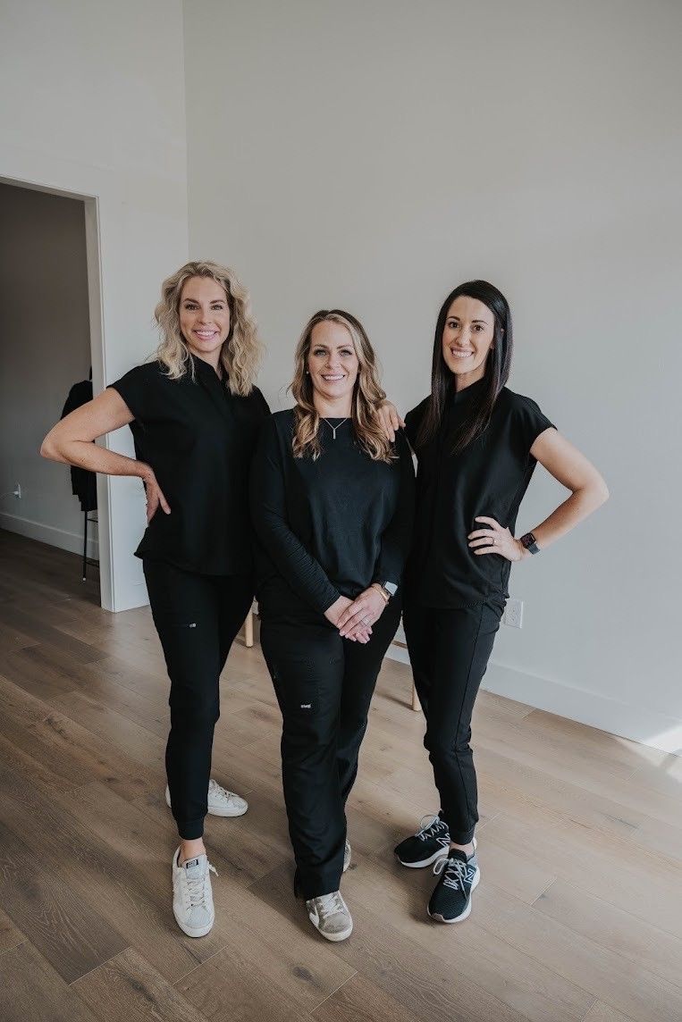 Three women in black scrubs are standing next to each other in a room.