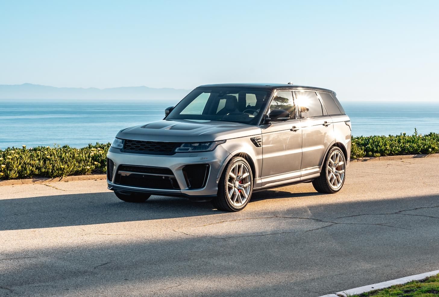 Silver SUV parked on a seaside road with ocean and distant mountains in the background