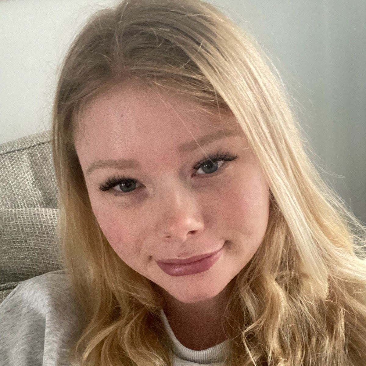 Blonde woman with a slight smile, wearing a grey sweatshirt, indoors.