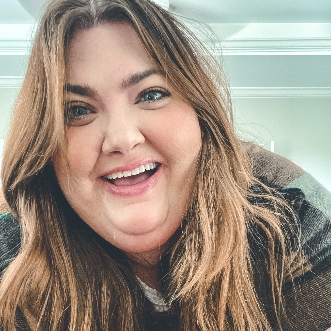 Woman with long brown hair, smiling with wide eyes, wearing a plaid shirt.