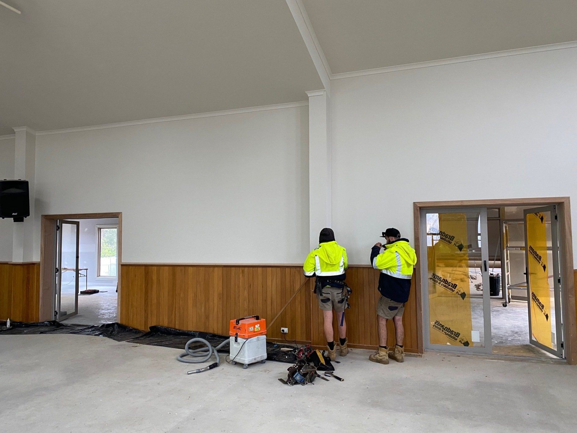 Two workers in high-vis vests install wood paneling inside a building.
