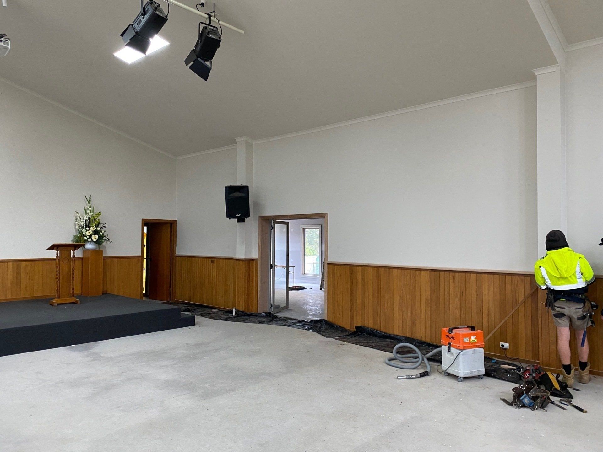 Interior of a church being renovated. A worker in safety gear stands near the wall.