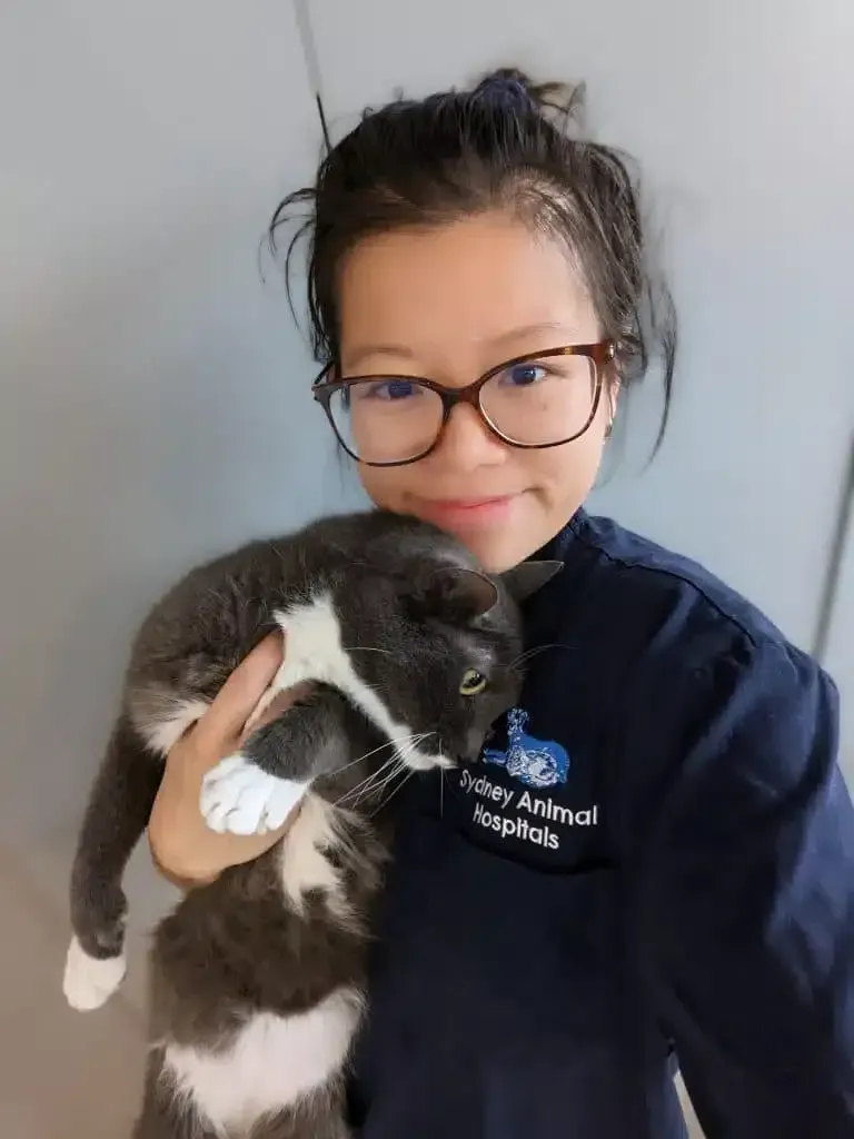 Woman in glasses holding a gray and white cat, indoors.