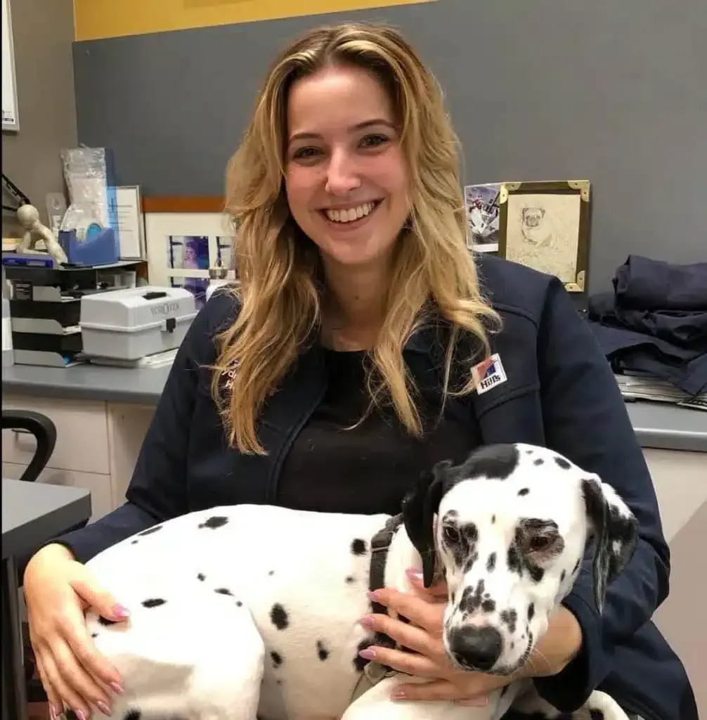 Woman in a navy jacket smiles, petting a Dalmatian dog in an office setting.