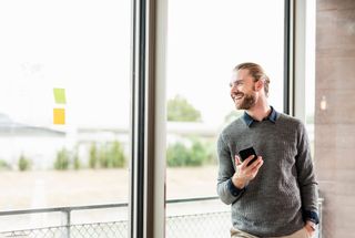 A man is standing in front of a window holding a cell phone.