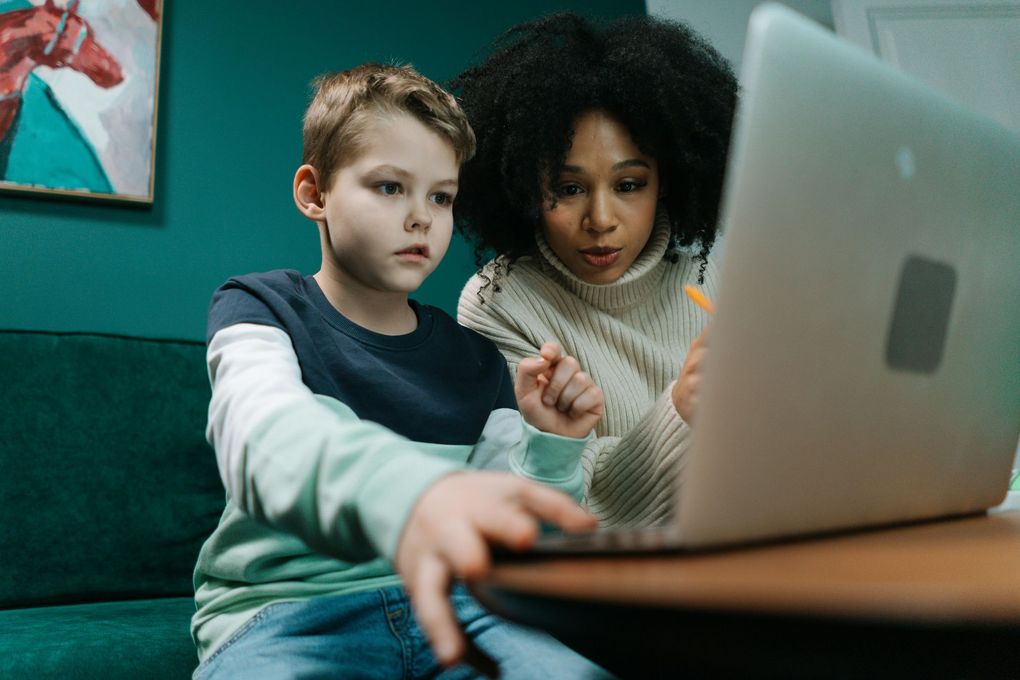 A woman and a boy are sitting on a couch looking at a laptop computer.