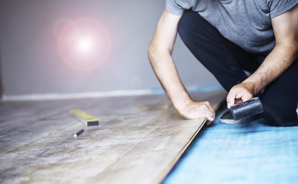 a man is kneeling on the floor while installing a wooden floor .