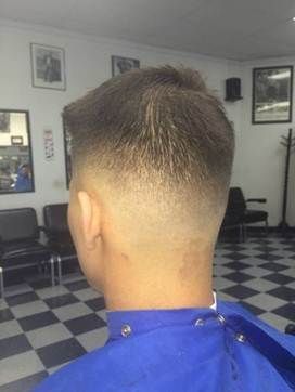 A person's hair, a high fade haircut with dark hair on top, in a barbershop.