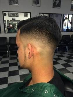 Man with a side part, faded haircut, sitting in a barbershop with a checkered floor.