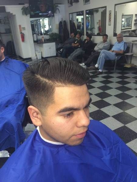 Man in a barber chair getting a haircut with others waiting in a shop.