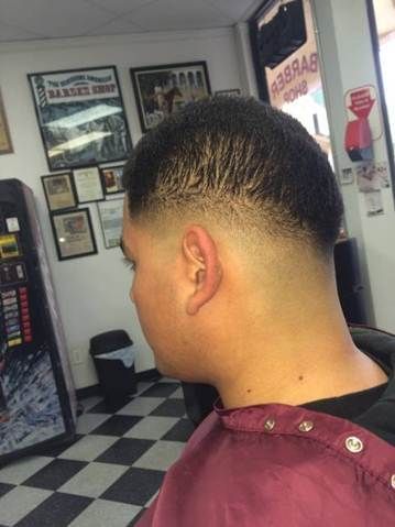 Man with a faded haircut at a barber shop, wearing a burgundy cape, with checkered floors.