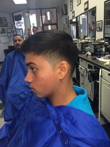 A person in a barber shop with a faded haircut, wearing a blue smock.