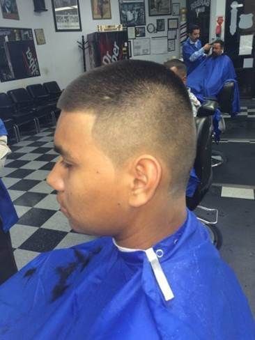 Man in a barber chair getting a haircut. He wears a blue cape. Barber shop interior with checkered floor.