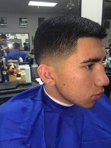 Man with a faded haircut, blue cape, looking away. In a barber shop.