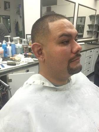 Man in a barber's chair with a fresh haircut and goatee. He's wearing a white smock in a barbershop.