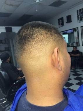Man's close-cut haircut, back view, in a barbershop. Faded sides, short top, blue clothing.
