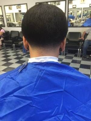 Person in a blue smock getting a haircut in a barbershop; faded nape, black hair.