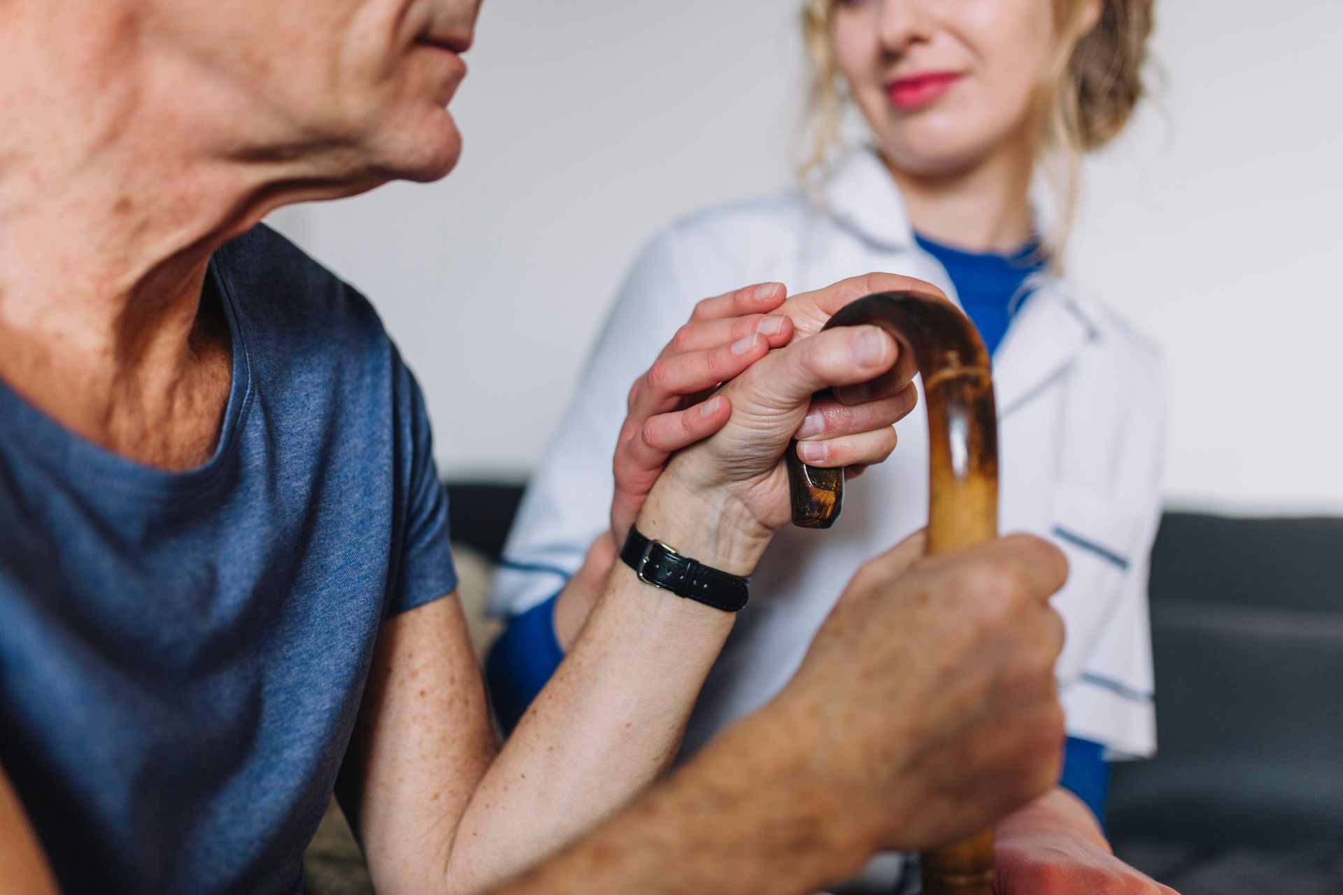 A person holds a walking cane, while another person's hand rests gently on top of theirs in a supportive gesture.