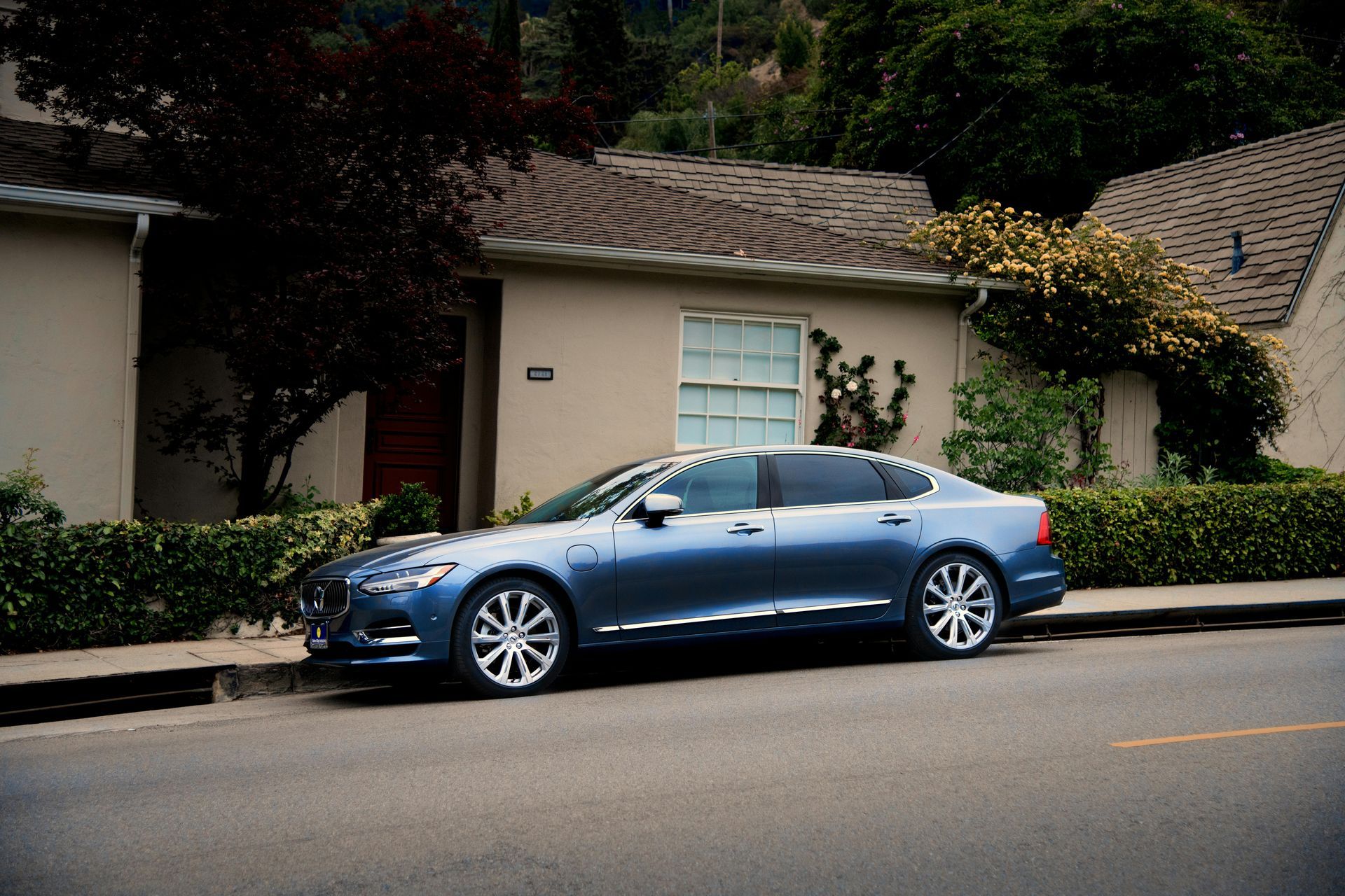 A blue luxury sedan parked on a residential street in front of a house with a tiled roof.