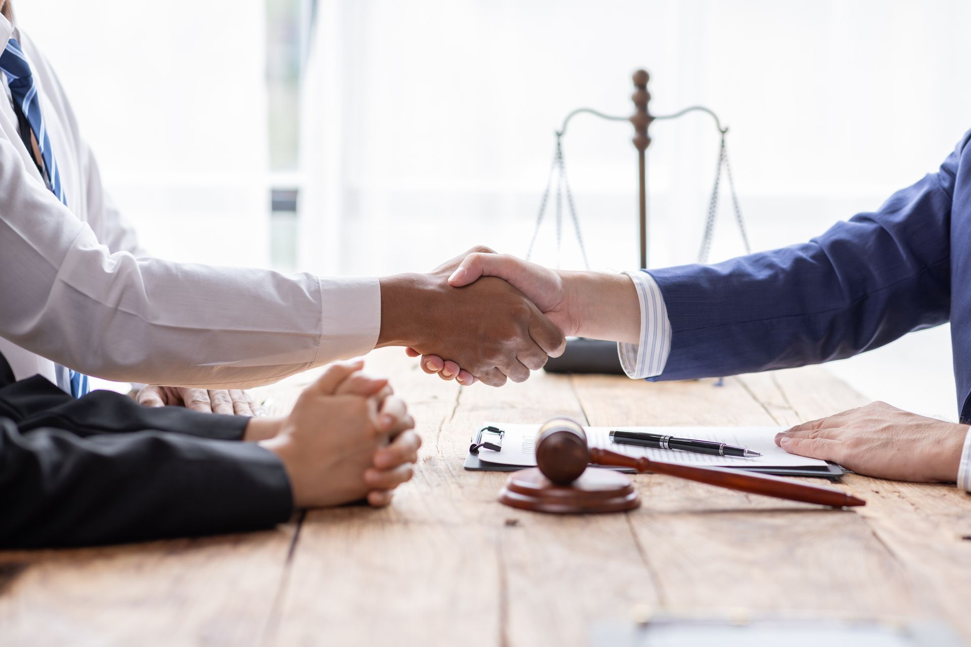 Two people shaking hands over a wooden table, gavel and papers in front.