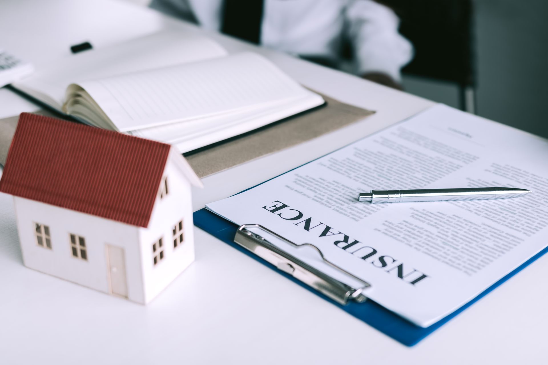 Model house next to insurance document with pen and open notebook on a white table.