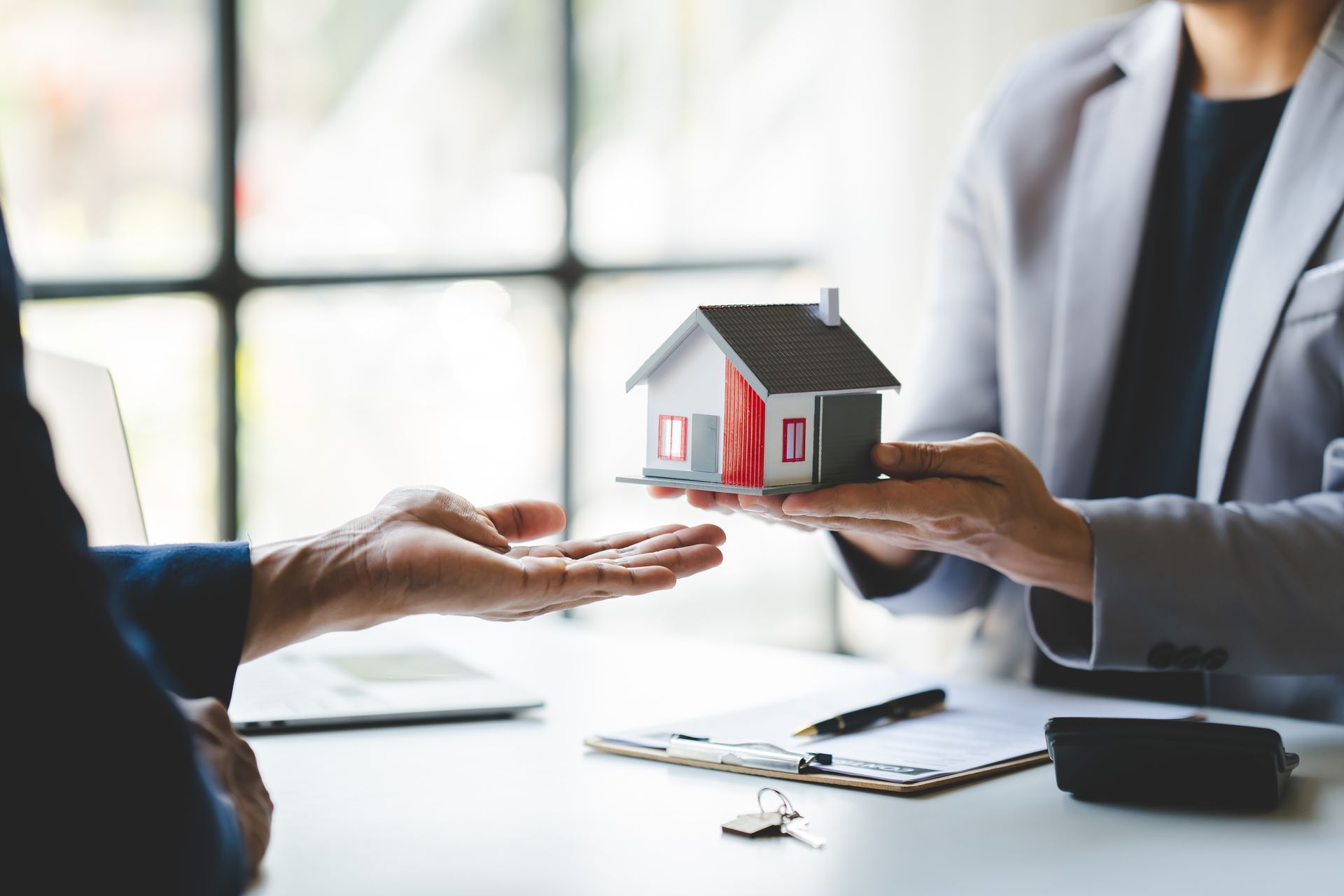 Person handing a miniature house model to another person over a desk.