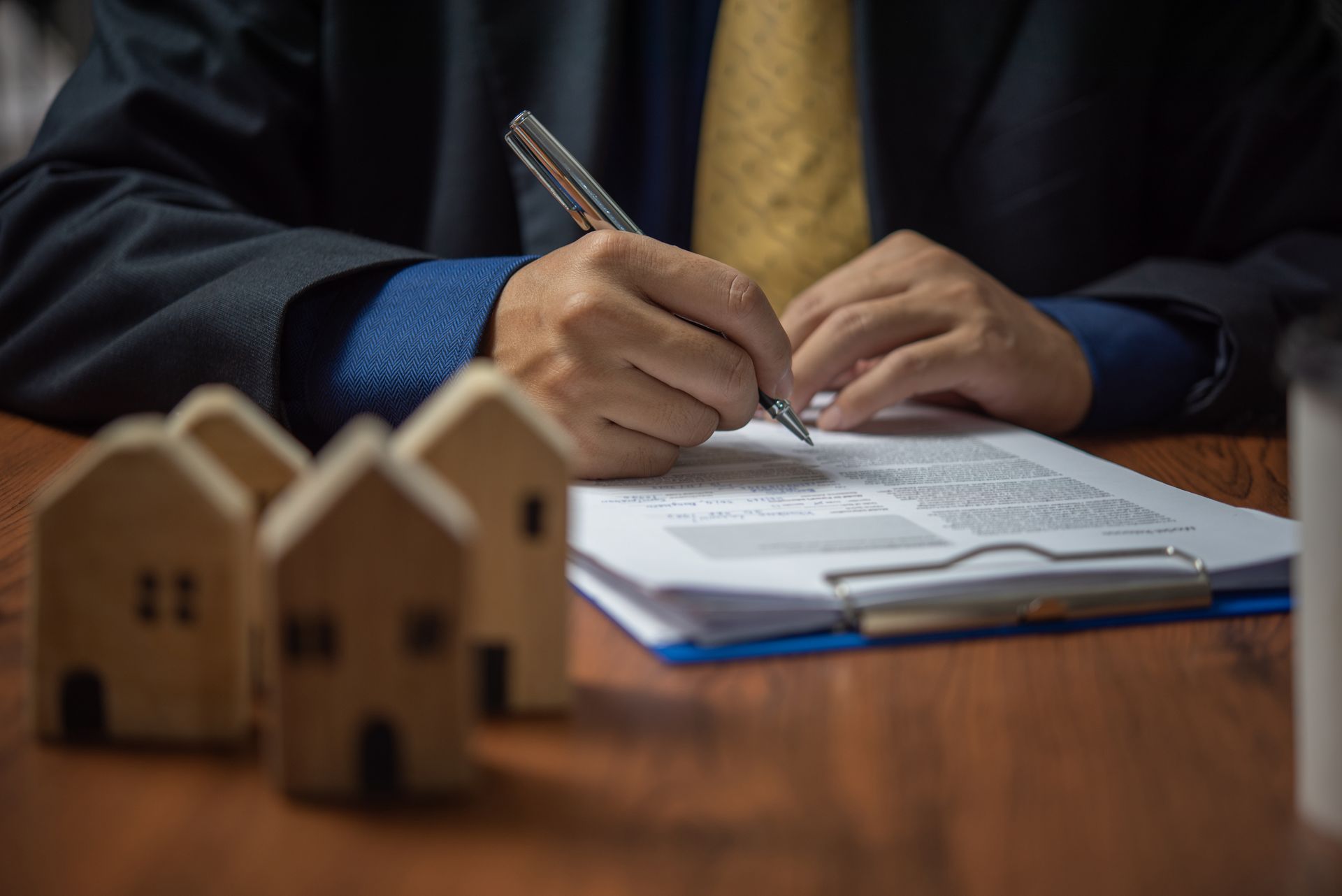 Person signing a document, with miniature house models on a wooden table.