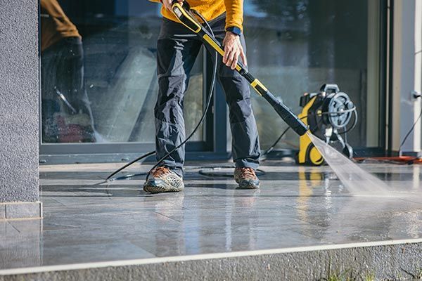 A man is using a high pressure washer to clean a concrete floor.