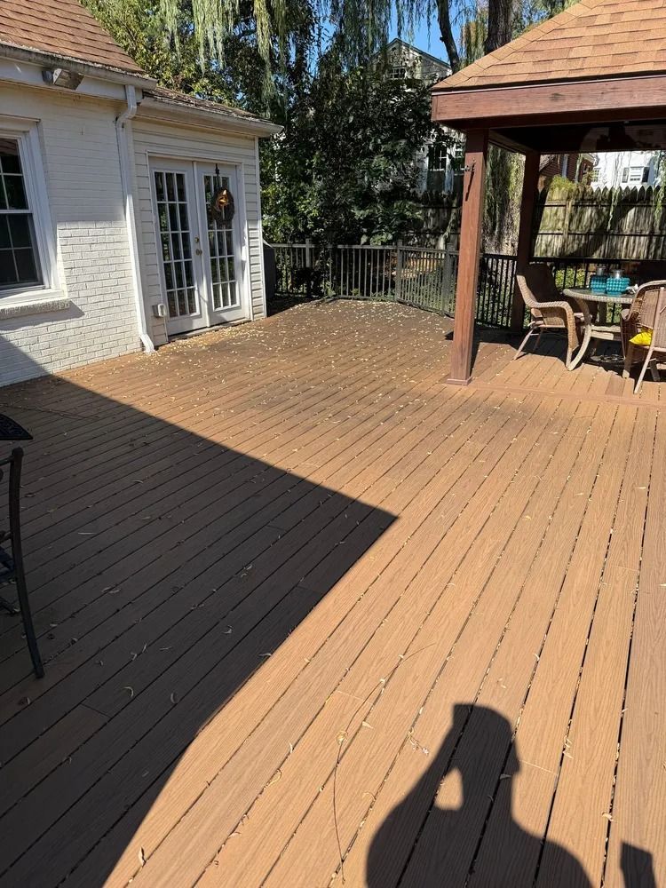 A wooden deck with scattered leaves leading to a white house with French doors and a nearby shaded gazebo.