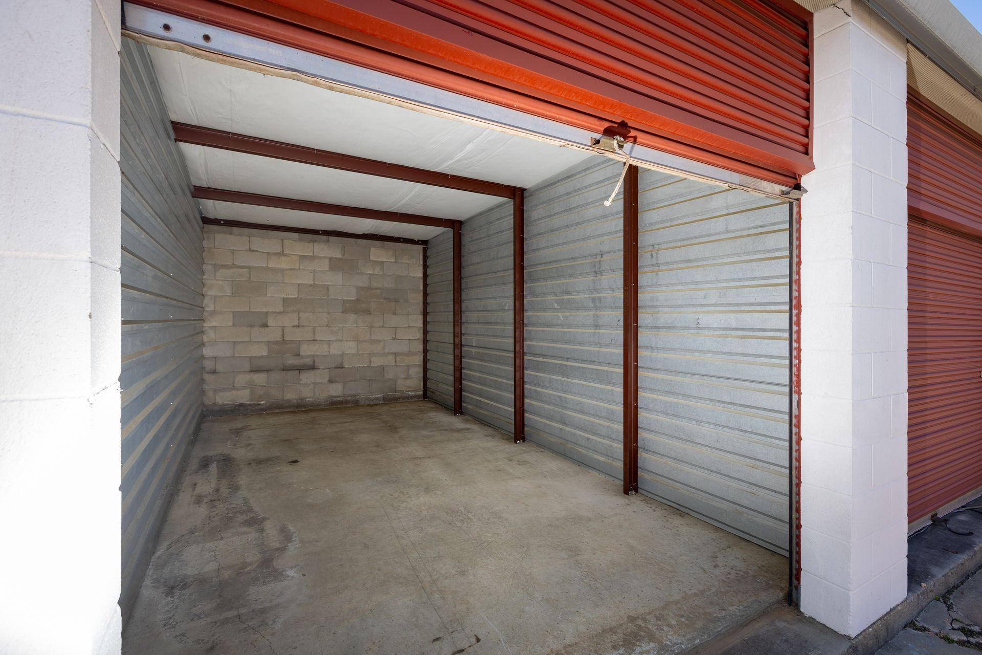 Empty storage unit with red metal door and cinder block back wall. Empty storage unit with red metal door and cinder block back wall.