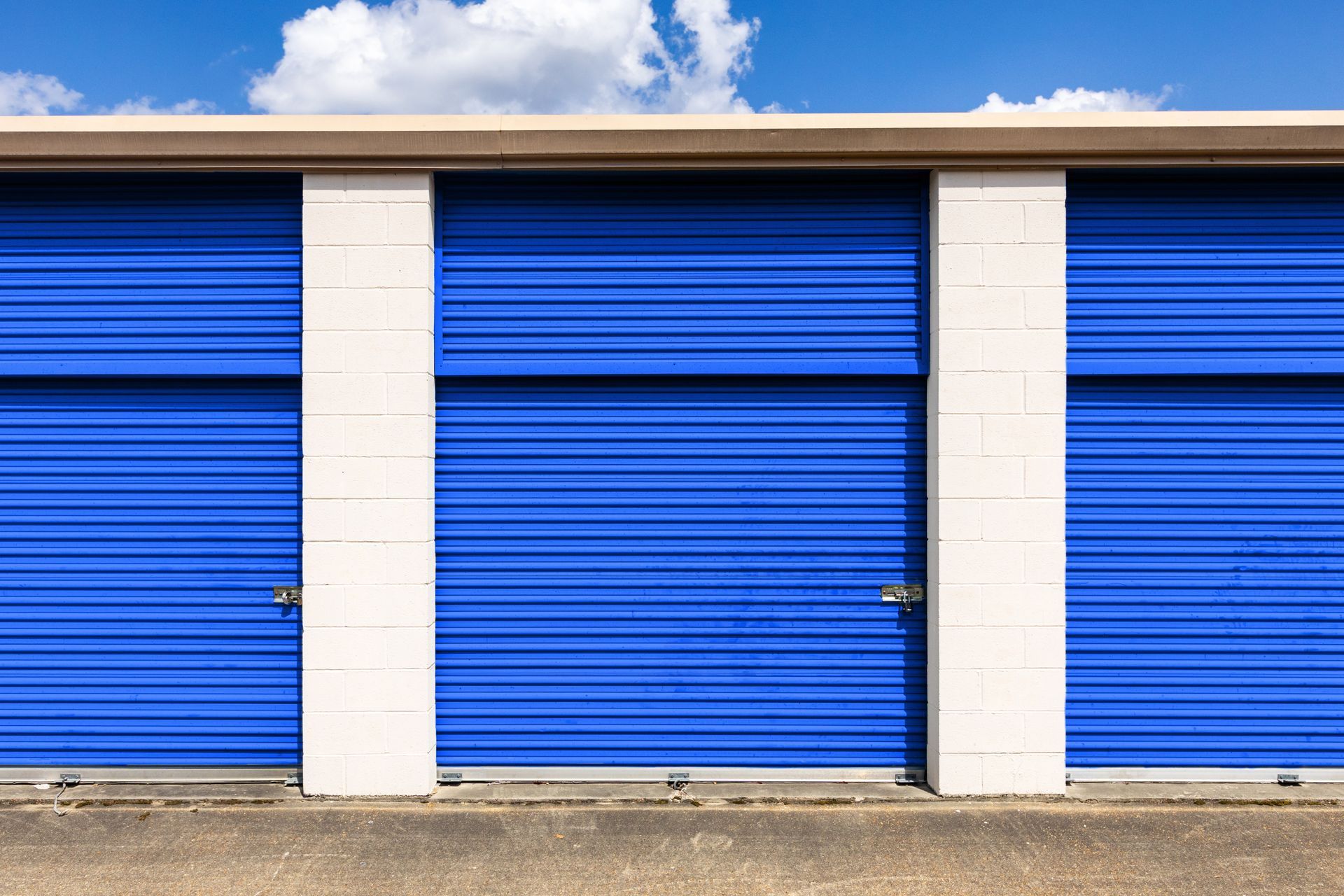 Blue storage unit doors with white pillars and a blue sky in the background. Blue storage unit doors with white pillars and a blue sky in the background.