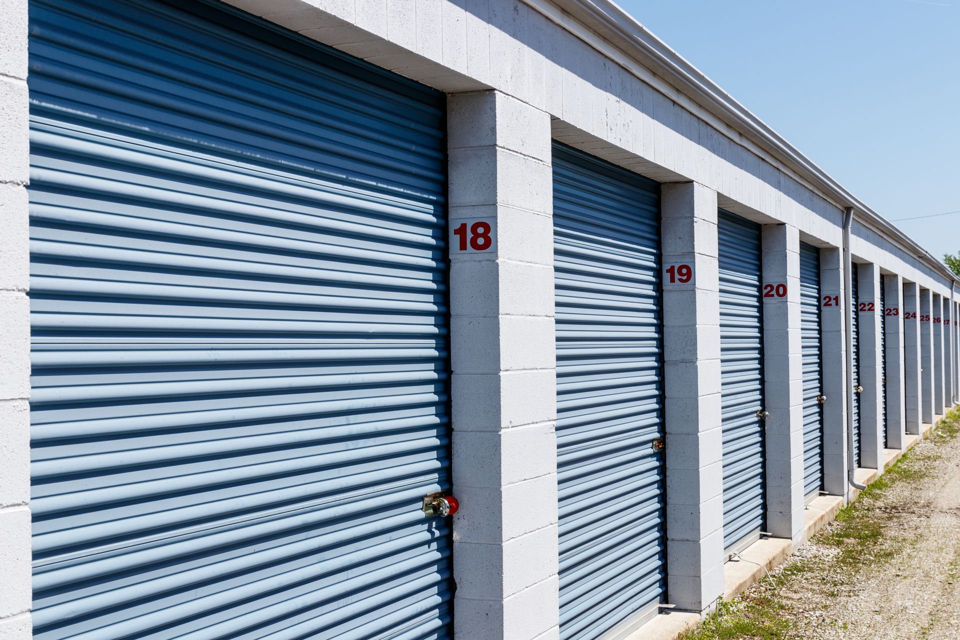 Storage units with blue metal doors, numbers 18-22 in red, along a cement structure. Storage units with blue metal doors, numbers 18-22 in red, along a cement structure.
