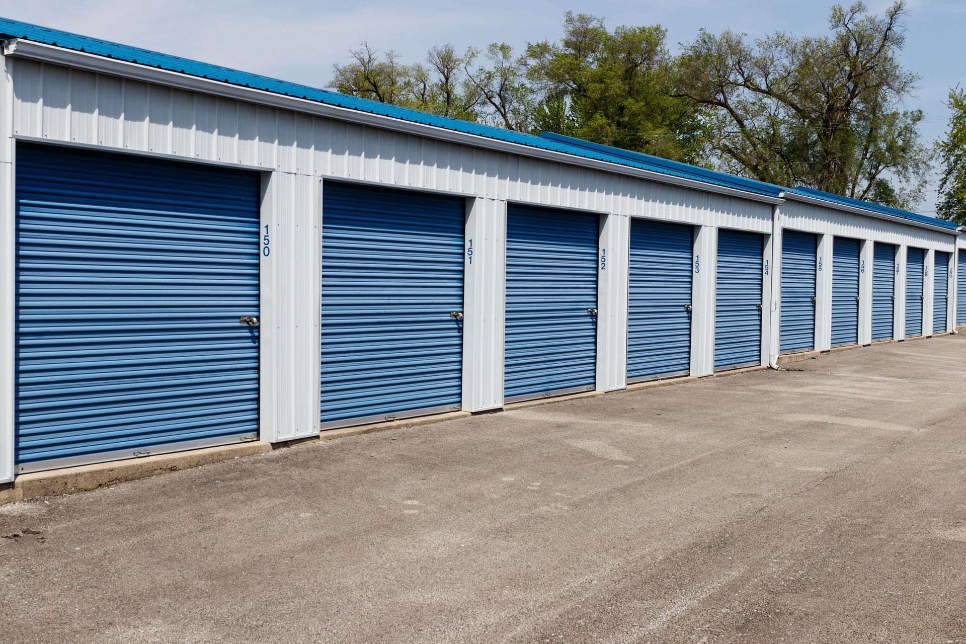 Blue storage units with white trim, set on asphalt, with a blue roof against a sunny sky. Blue storage units with white trim, set on asphalt, with a blue roof against a sunny sky.