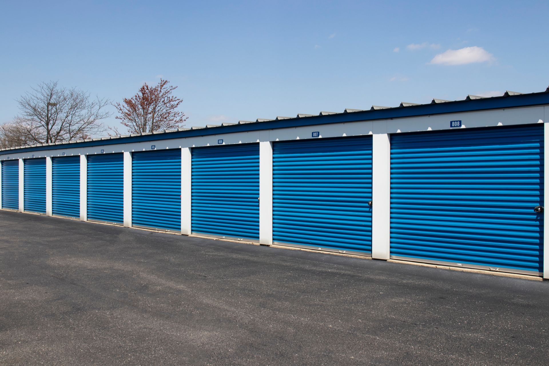Row of blue storage unit doors with white trim under a clear sky. Row of blue storage unit doors with white trim under a clear sky.