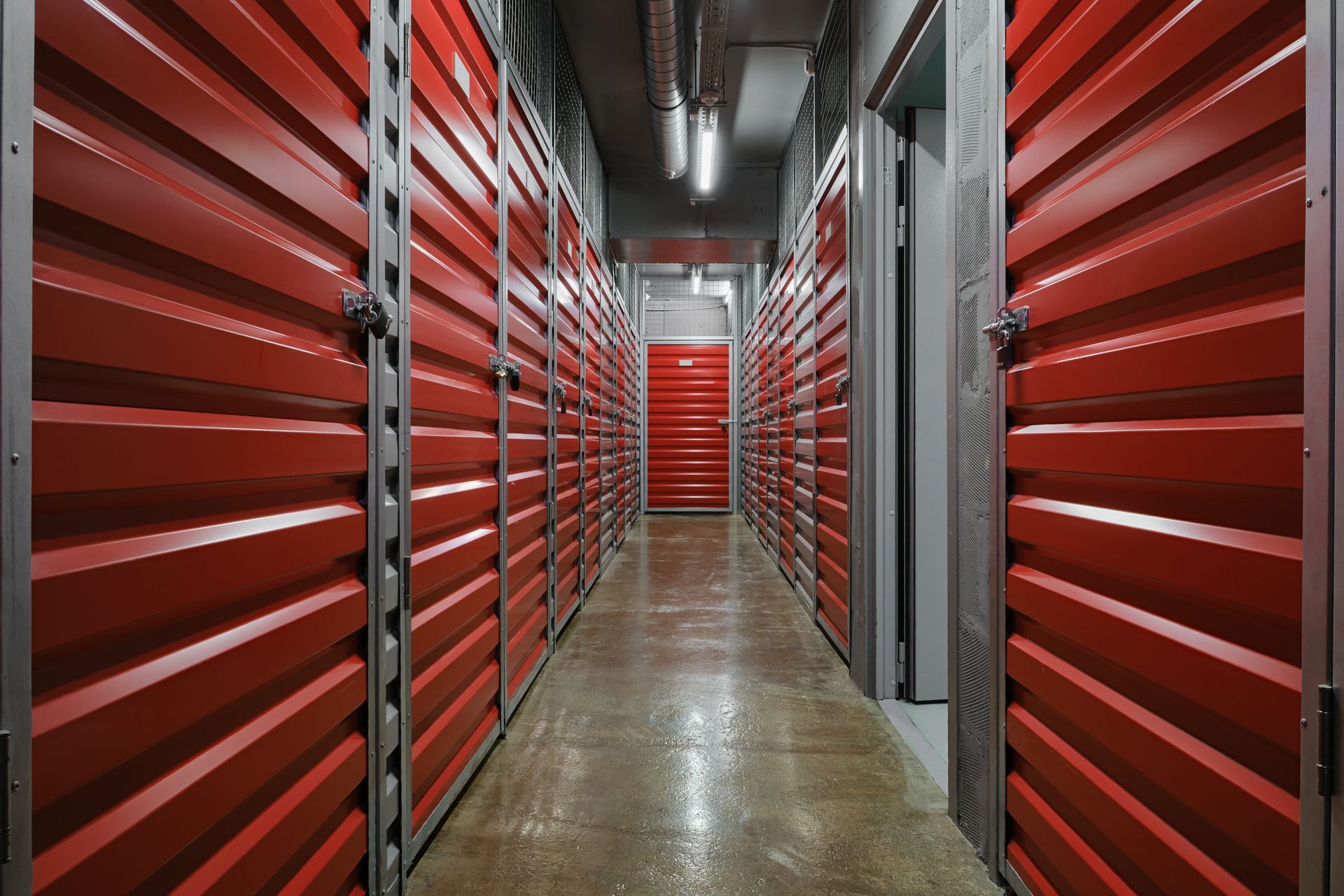Interior view of storage units, red doors in a long hallway, lit by overhead lights. Interior view of storage units, red doors in a long hallway, lit by overhead lights.