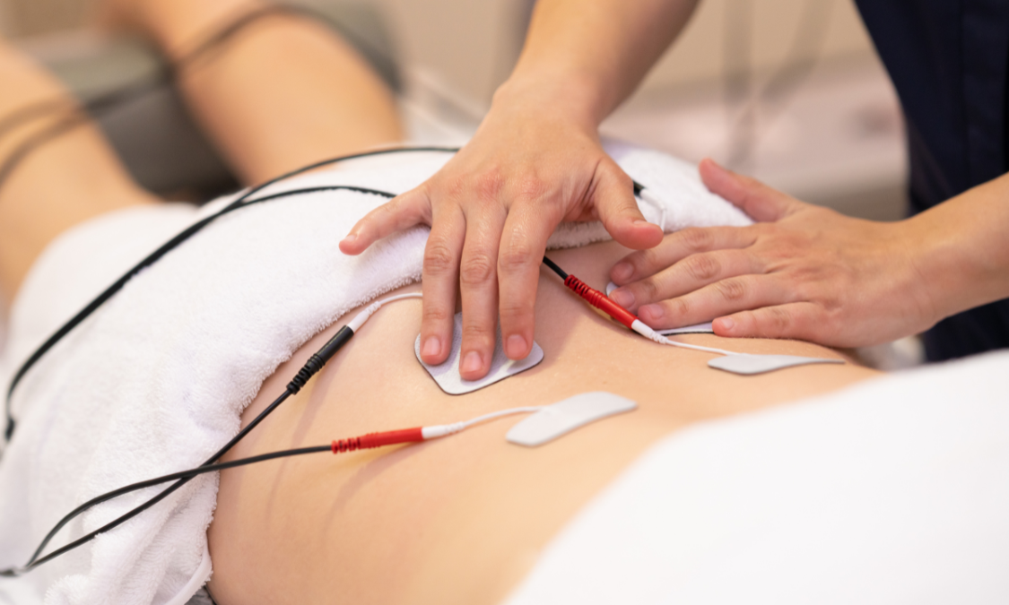 Person receiving electrical stimulation on their abdomen with hands.