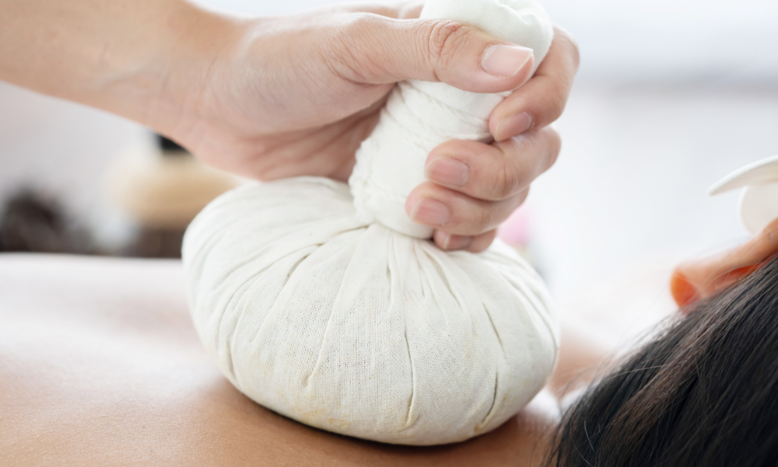 Person receiving a massage with a warm herbal compress on their back.