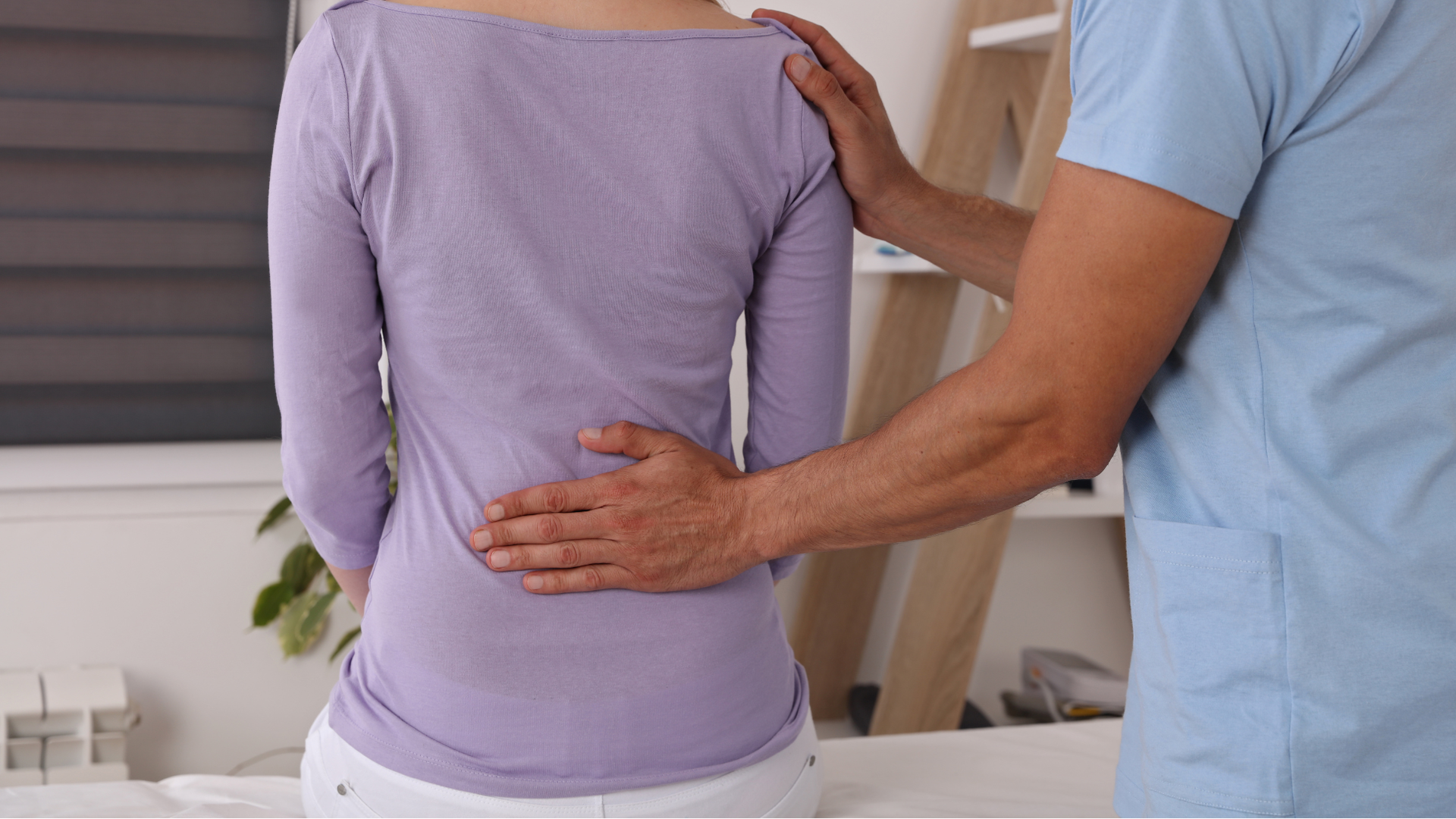 A woman in a purple shirt has her back examined by a healthcare professional.