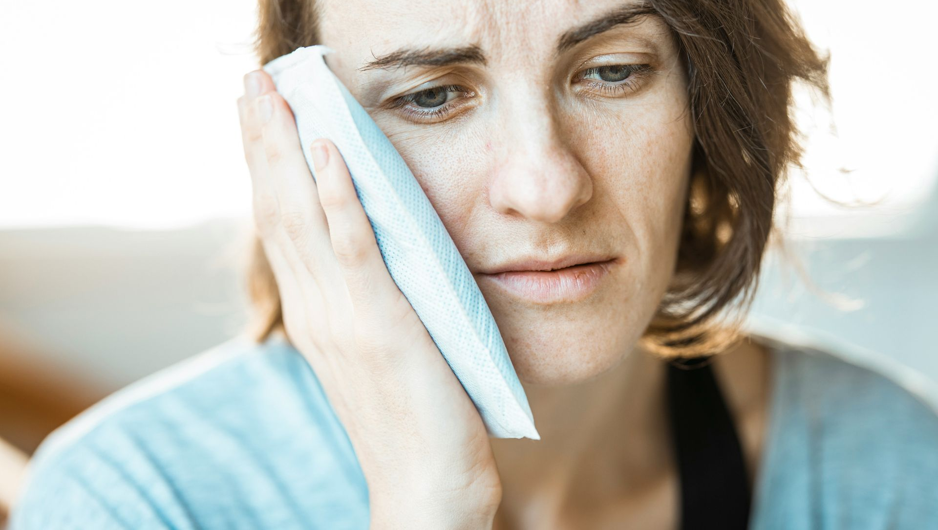 Woman with sad expression holding ice pack to her cheek, presumably for pain relief.
