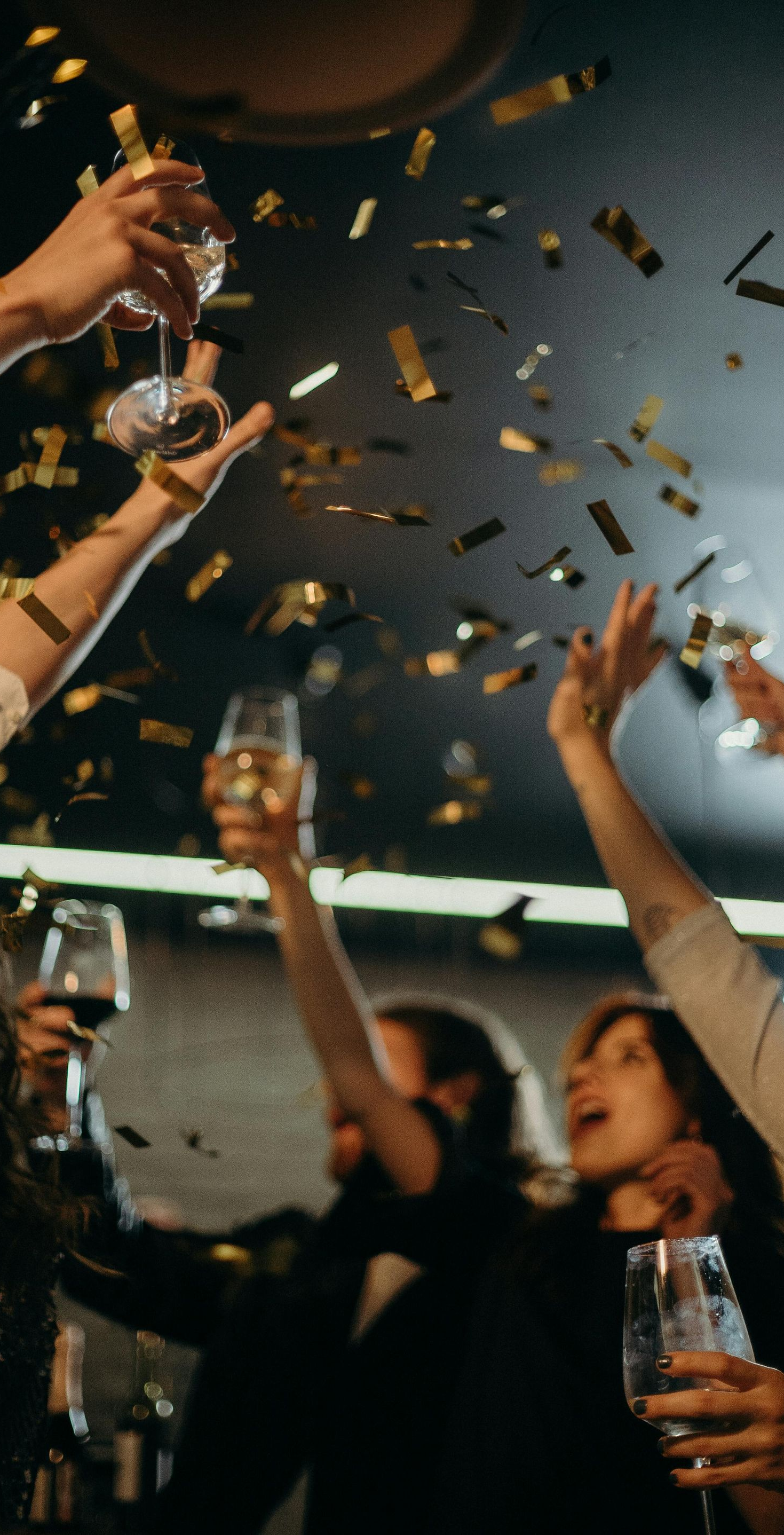 People toasting with wine glasses under falling golden confetti.