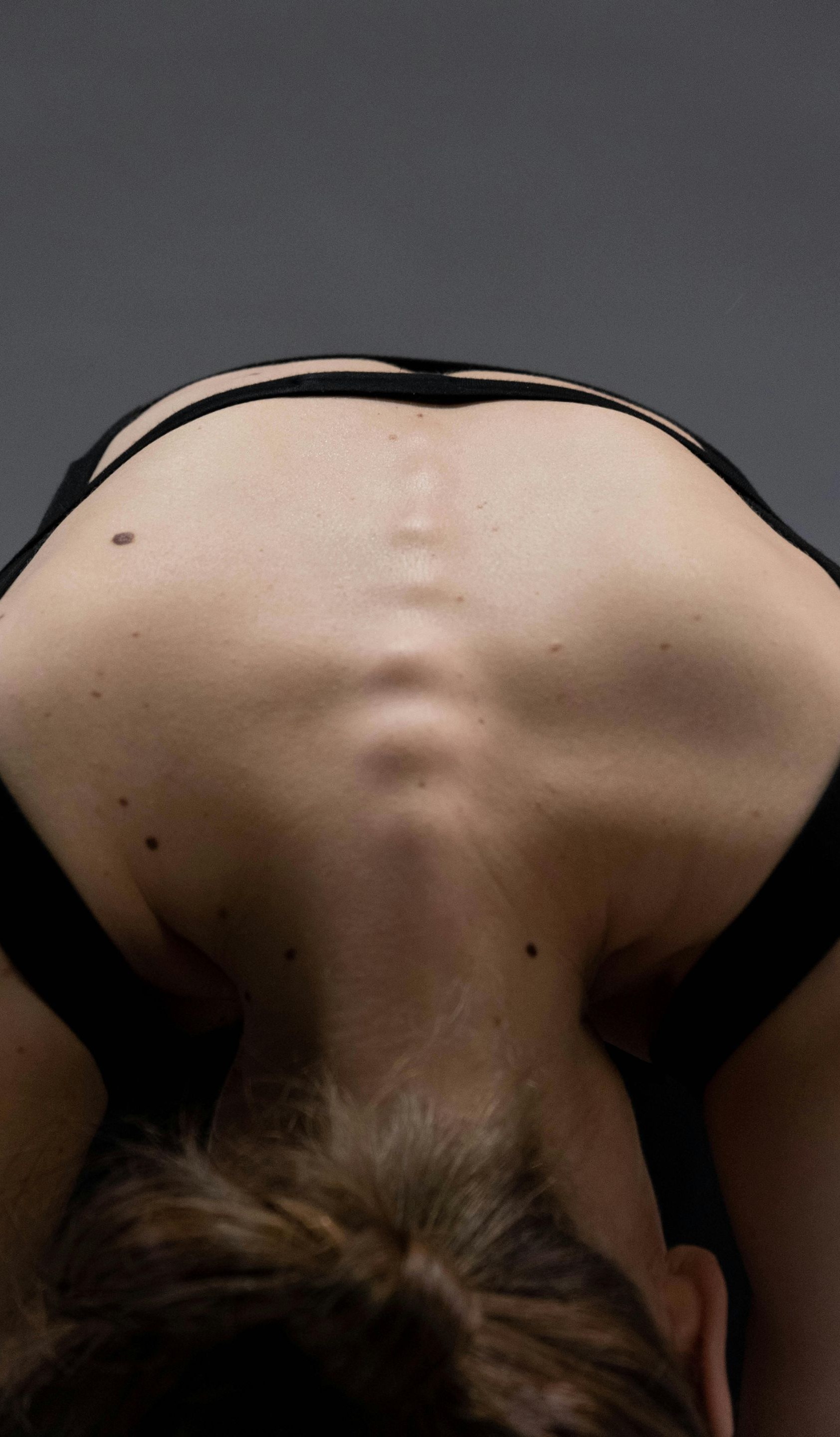 Person bending forward, back arched, showing spine and shoulder blades. Wears a black sports bra.