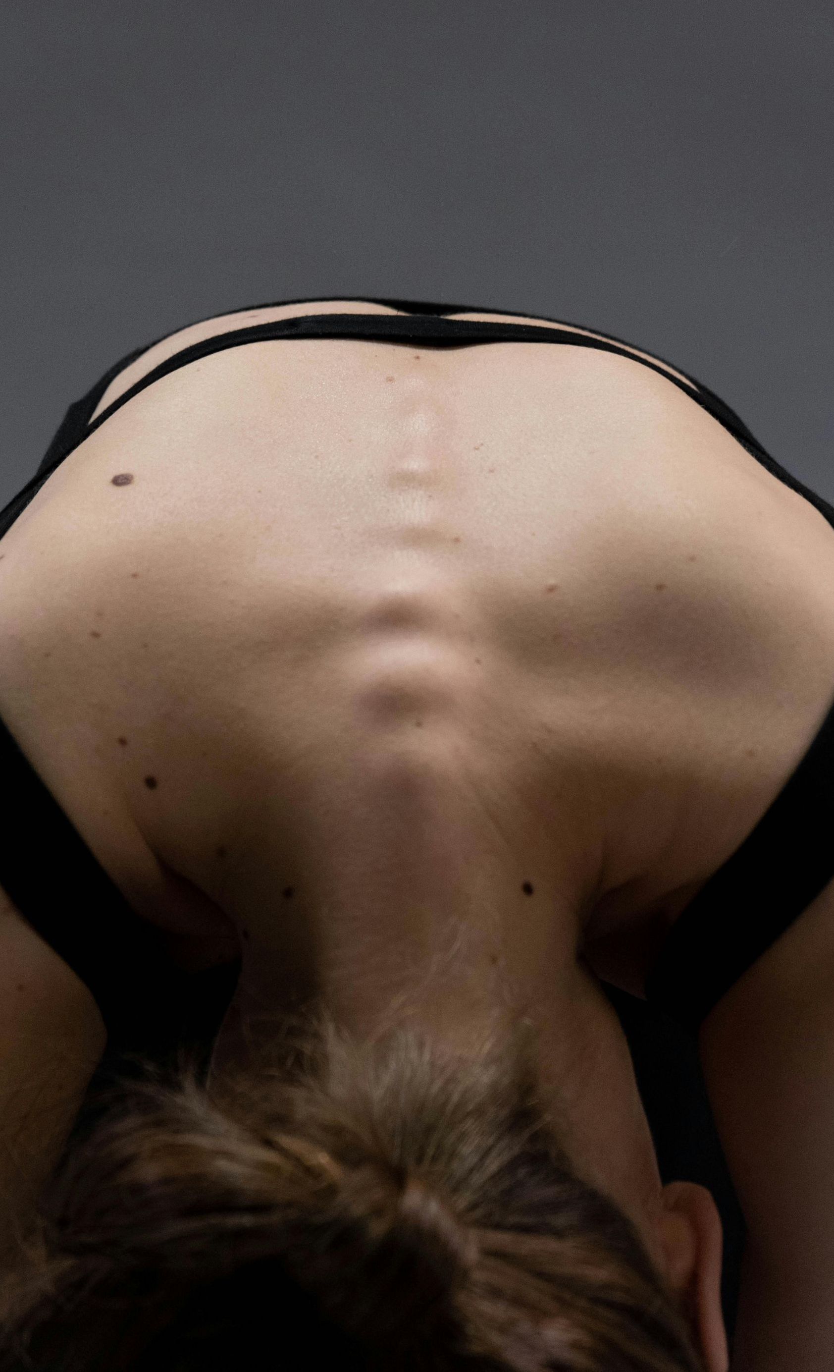 Person bending forward, back arched, showing spine and shoulder blades. Wears a black sports bra.